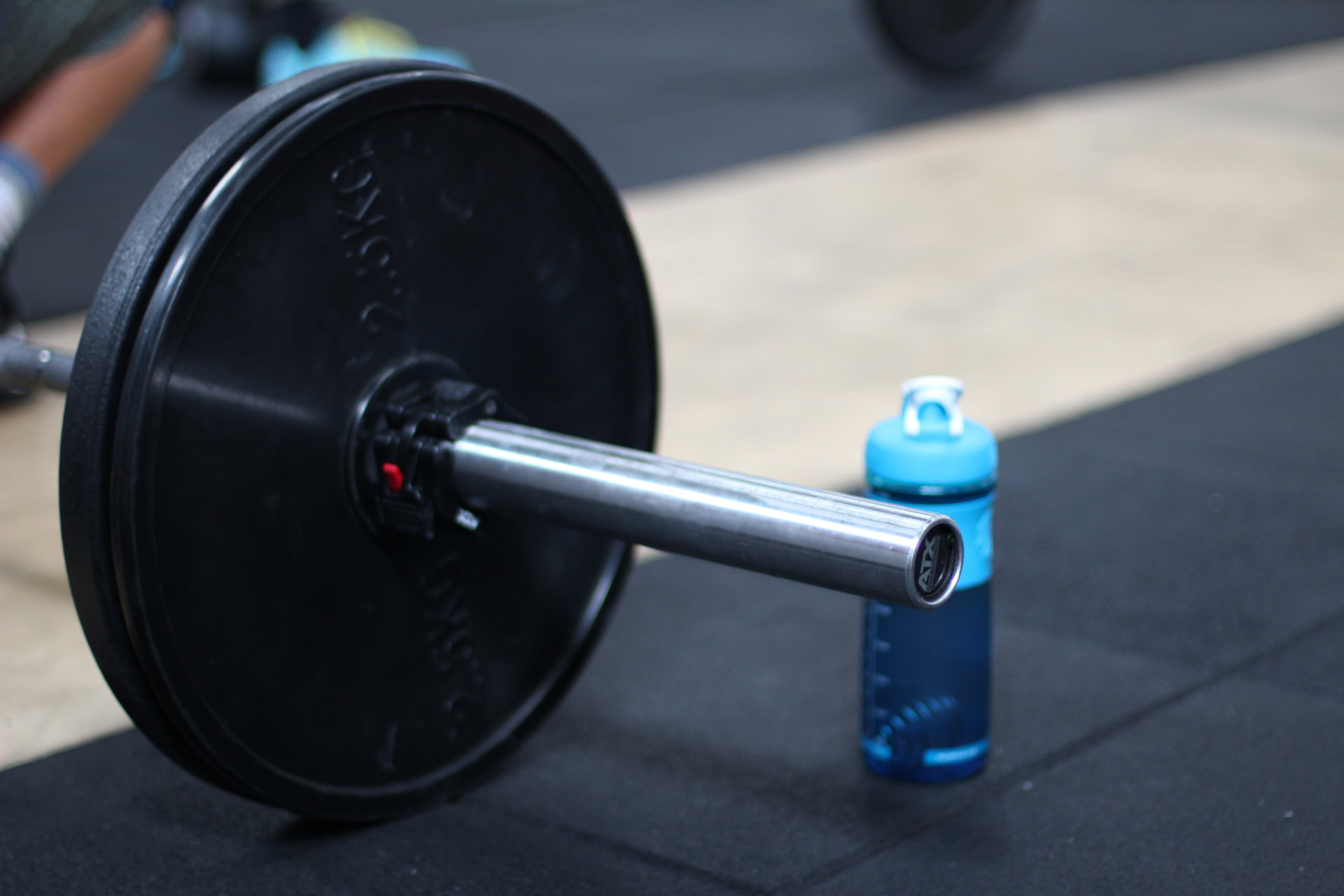 A loaded barbell resting on the gym floor beside a water bottle